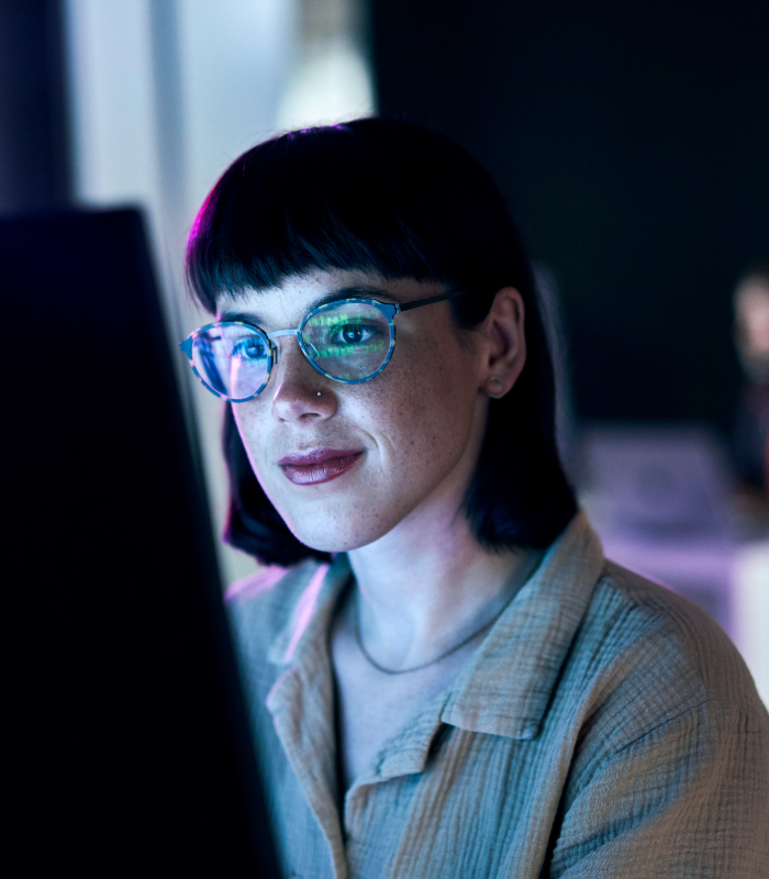 Woman wearing glasses working at night looking at monitor