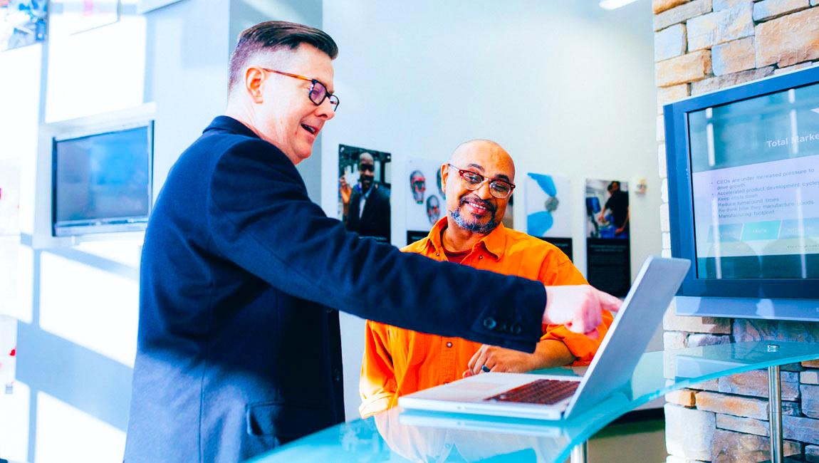 Two male business colleagues smiling and looking at laptop