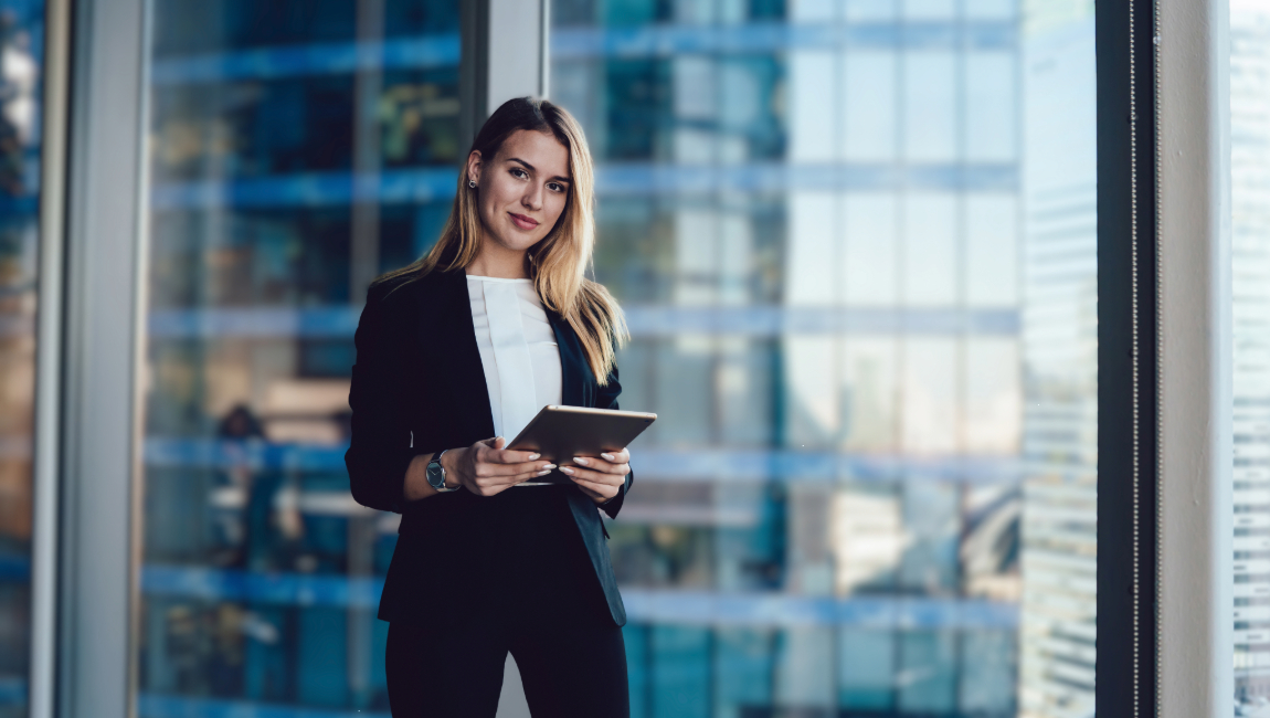 Young businesswoman standing in front of large office window holding a tablet
