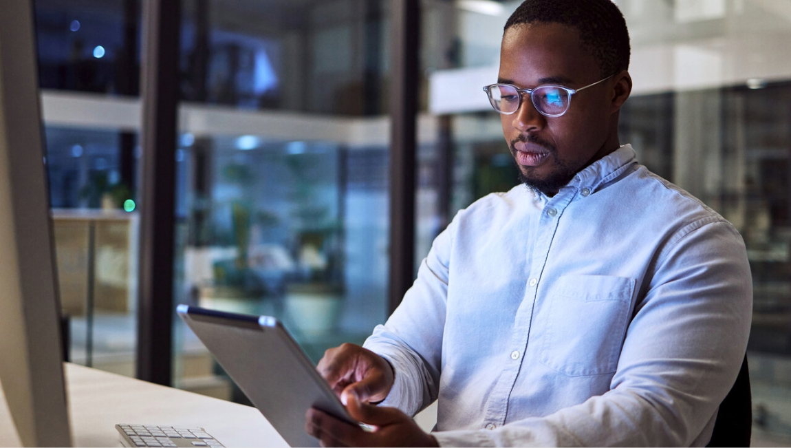 Man sitting at a desk at night reading on a tablet