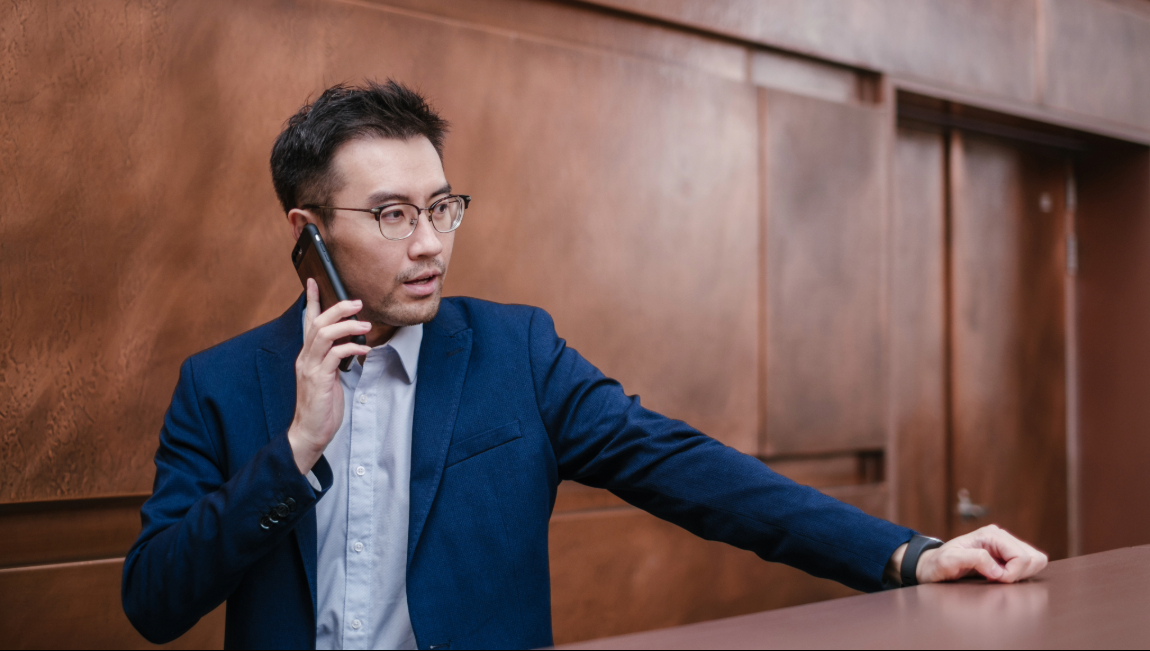 Businessman standing in front of brown wall while talking on mobile phone