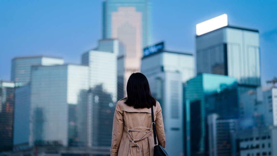 Woman wearing trench coat facing downtown skyscrapers