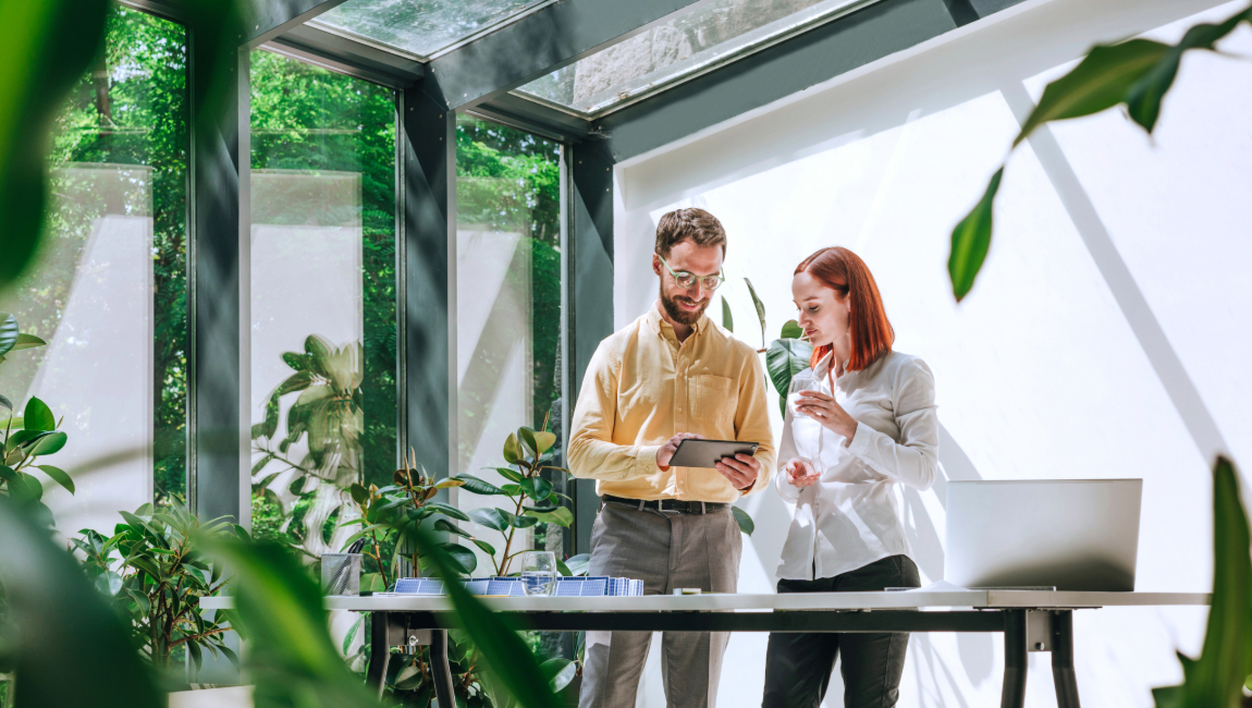 Male and female colleagues standing in office with lots of plants while looking at tablet