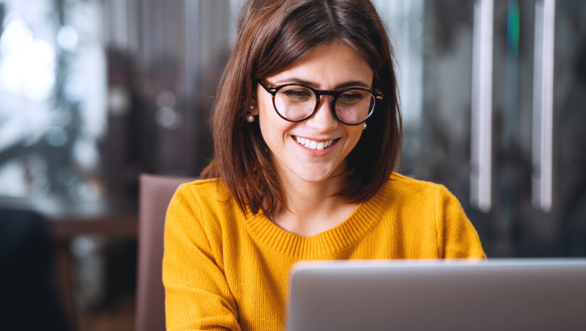 Happy businesswoman wearing glasses looking at laptop at work