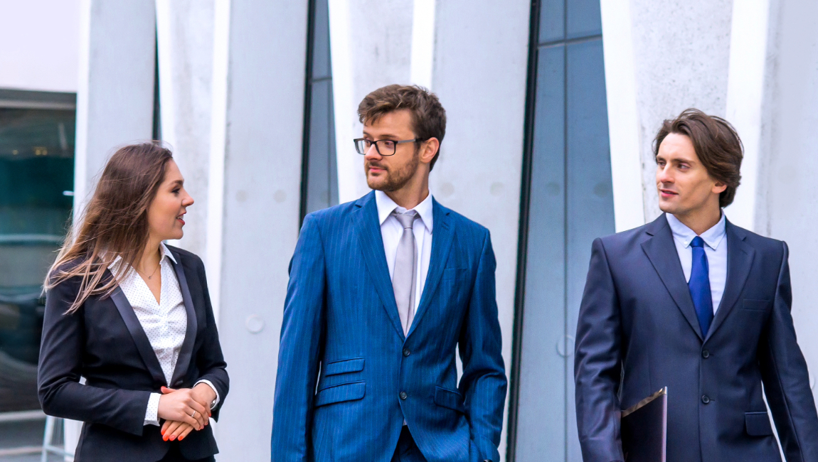 Three colleagues dressed in business clothing walk outside a modern office building